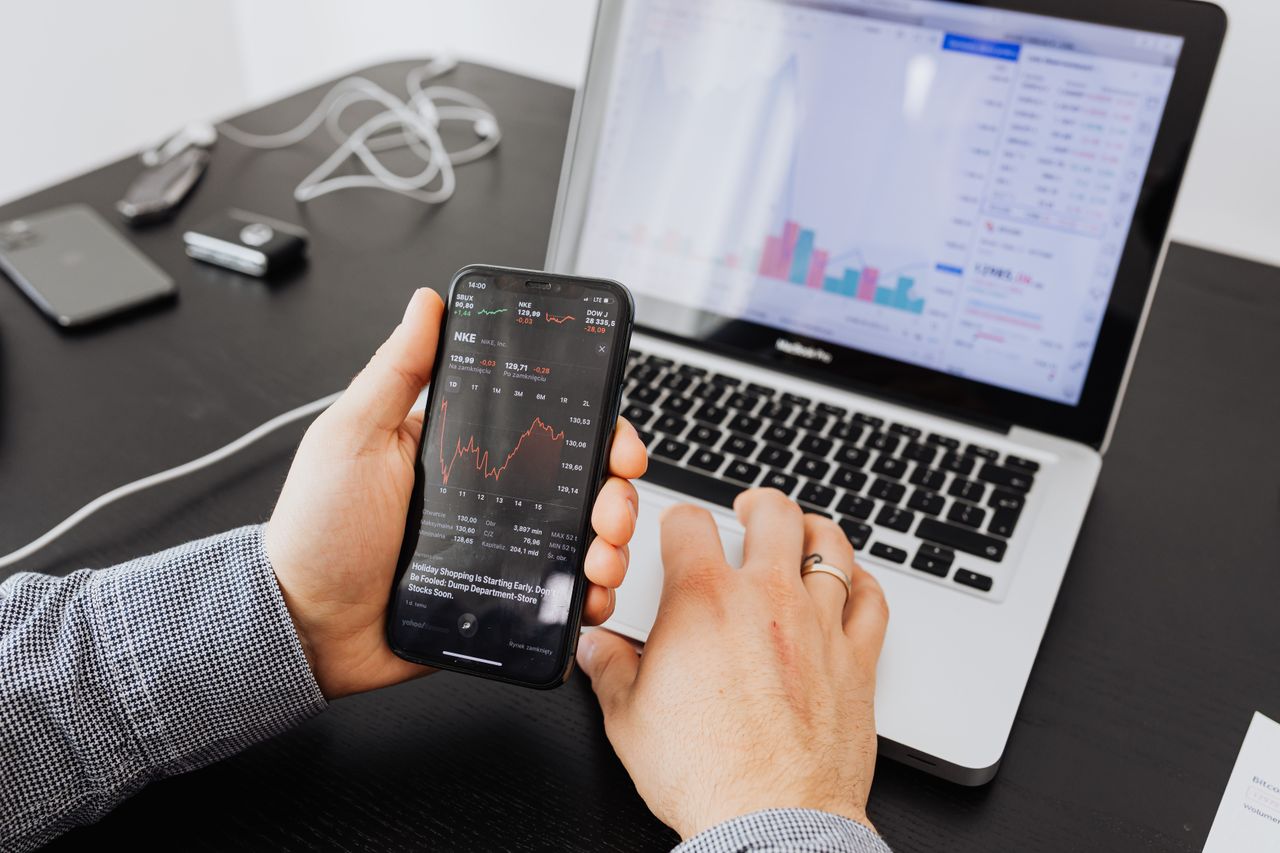 Home Person analyzes stock data with a smartphone and laptop, indoors.