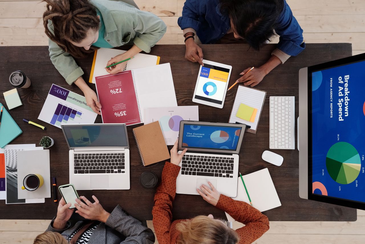Contact A diverse team collaborating on digital marketing strategies at a desk, using laptops and tablets.