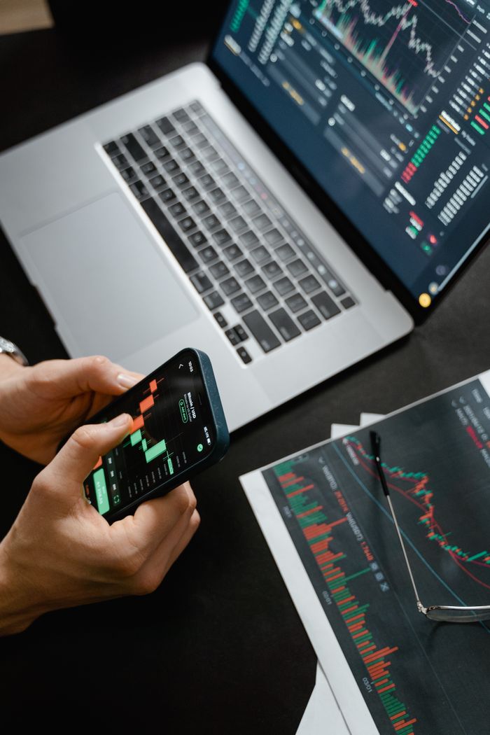 Home Hands holding phone with financial graph, laptop in view.